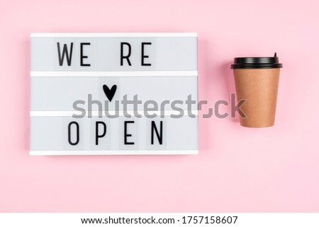 Information text WE ARE OPEN on a lightbox on a pink background with an eco coffee cup. Message for customers from business. Opening of hotels, restaurants, cafes and the entertainment industry after 