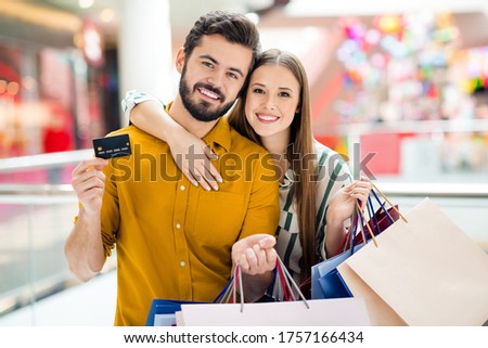 Photo of two people cheerful lady handsome guy couple enjoy free time hold many bags use credit card salary shopping center hugging wear casual jeans shirt outfit indoors