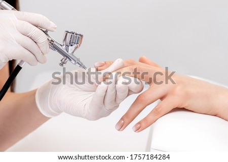 Manicure master is painting finger nails in beige color using airbrush. Woman getting fingernail manicure. Royalty-Free Stock Photo #1757184284
