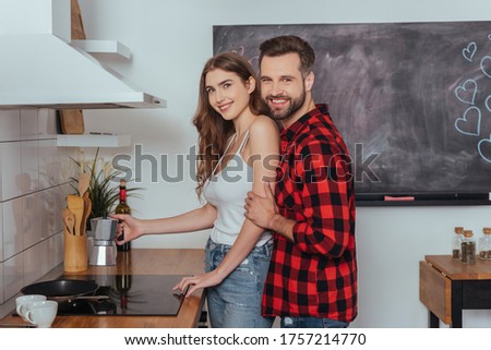 happy young couple smiling at camera while making coffee in geyser coffee maker