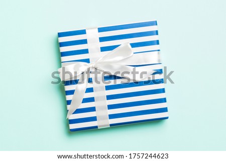 Gift box with white bow for Christmas or New Year day on blue background, top view with copy space.