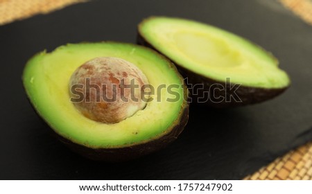 ripe halved avocado with bone on black stone board