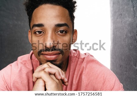 Photo of bearded african american man posing and looking at camera isolated over grey wall with white light
