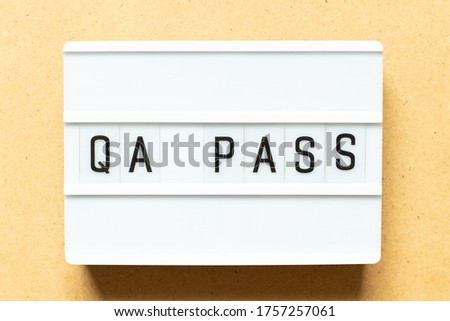 Lightbox with word QA (Abbreviation of Quality Assurance) pass on wood background