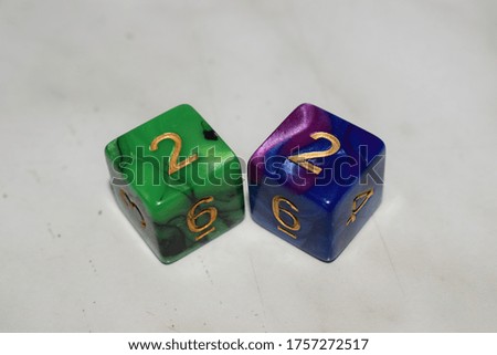 A green and black dice showing the number 2 and a blue and purple dice showing the number 2 on a white table