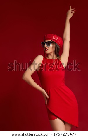 elegant classy brunette young woman in white trendy sunglasses, red leather beret and dress posing in studio