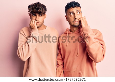 Young gay couple wearing casual clothes looking stressed and nervous with hands on mouth biting nails. anxiety problem. 