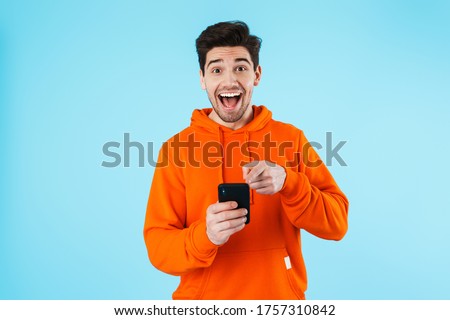 Image of a happy surprised young bristle man isolated over blue wall background using mobile phone.