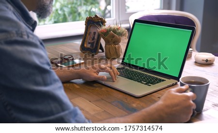 Businessman drinking coffee in his office and reading something on the computer.Shot of a man typing on a computer laptop with a key-green screen. Man hand typing laptop with green screen.
