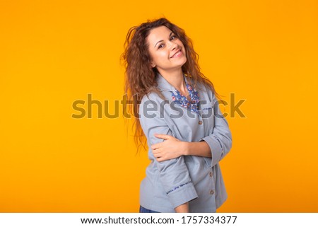 Excited young woman with curly hair in blue homewear, widely smiling having fun. Isolated on yellow background. Copy space.