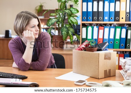 Young worker with regret looking at box with personal belongings on table