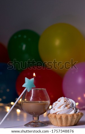 cupcake with a blue star-shaped candle and a glass with a brown liquid - liquer. On the background of multi-colored balloons and lights. party, birthday concept. Copy space. . High quality photo