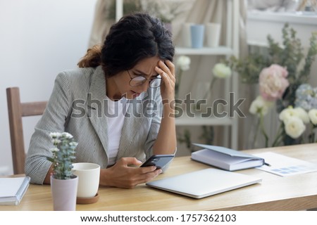 Depressed unhappy young woman sit at table at home look at cellphone screen frustrated by unpleasant news online, upset millennial female confused disappointed by bad negative response on smartphone Royalty-Free Stock Photo #1757362103