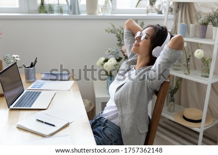 Calm young woman in headphones relax in chair at workplace distracted from computer work listen to music, happy female in headset enjoy good quality sound in earphones, rest at workspace at home Royalty-Free Stock Photo #1757362148