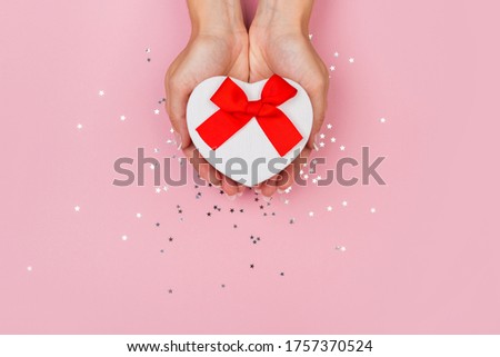 Women hands holding a gift or gift box decorated with confetti on a pink pastel table top view. Flat composition for birthday or wedding.