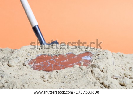 a shovel stuck in the sand there is a broken smartphone. dug up broken things in the sand
