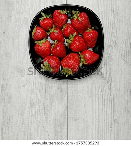 Fresh juicy red strawberries lying on a black plate in studio light

