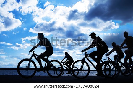 Image of sporty company friends on bicycles outdoors against sunset. Silhouette A lot phases of motion go of five 5  cyclist along shoreline coast. Reflection sun on water. Copy Space for inscription.