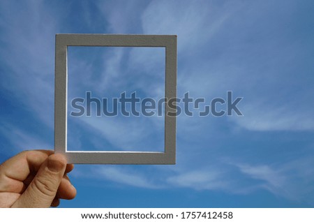 Hand holding a wooden frame on blue sunrise sky background. Care, safety, memory or painting concept.                       