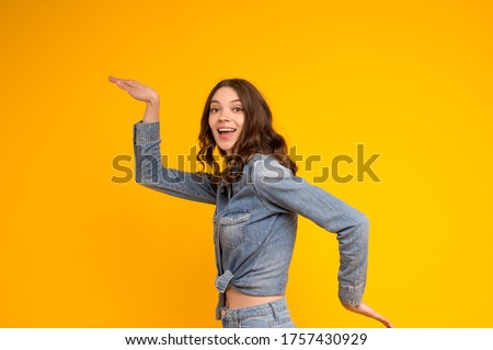 Funny smiling young brunette caucasian woman in denim shirt and jeans dancing with pleasure isolated on yellow background.Indoor portrait excited beautiful curly girl waving hands,celebrating winning