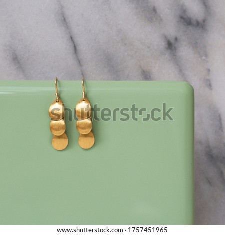 Earrings hanging from a green tile in front of a marble background. 
Jewellery setup. Jewelry fashion photography. Earrings fashion photography.