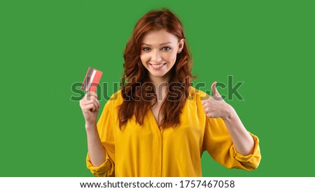 Happy Millennial Girl Holding Credit Card Gestruing Thumbs Up Approving Financial Banking Service On Green Studio Background. Panorama