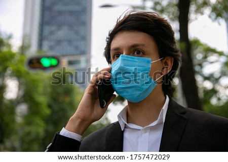 Stock photo of men talking on the mobile phone on the street. He is wearing a protective mask for the prevention of a virus. Coronavirus concept