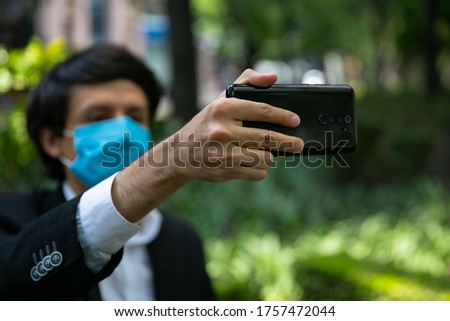 Stock photo of men using mobile phone in the street. He is wearing a protective mask for the prevention of a virus. Coronavirus concept