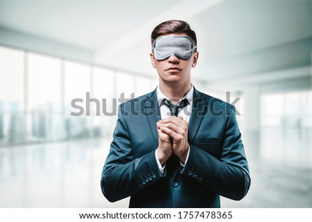 Portrait of a man in a business suit. He is praying while standing in the office. He has a sleep mask on his eyes. Blind business concept. Mixed media