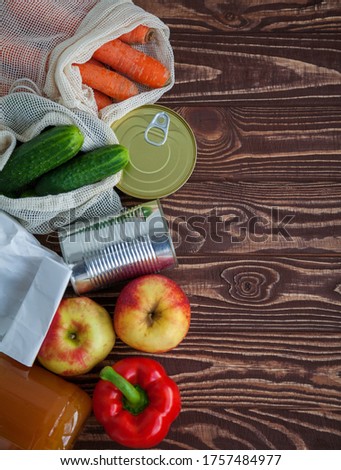 A set of different food products for home purveyance. Some of them are in reusable bags. Canned food, rice, fruits and vegetables on a wooden background. Copy-space, top view