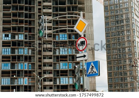 Road signs: main road, pedestrian crossing, stop is prohibited. In the background, the city under construction.