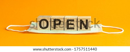 Word OPEN made with wood building blocks with medical mask, health concept background, yellow background.