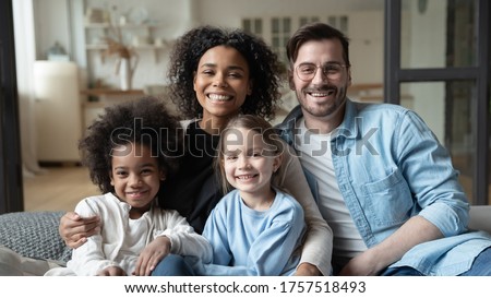 Multinational family married couple and daughters sit on couch looks at camera photo shooting feels happy. Cute multi-ethnic girls and parents portrait, homeowners, new home, prosperous future concept Royalty-Free Stock Photo #1757518493