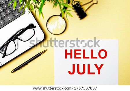 On the office desk is a laptop, glasses, a magnifier, a pen and a sheet of paper with the words Hello July
