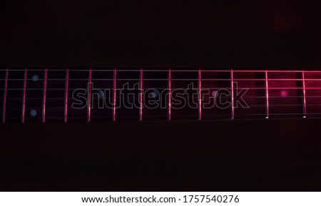 closeup to a six black electric guitar strings and wooden fretboards iluminated with red lights Instruments and music concept Royalty-Free Stock Photo #1757540276