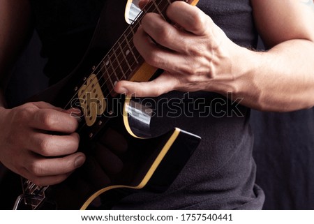 Closeup to a man wearing a black t-shirt playing a black and yellow electric guitar with wooden background. Rock & roll and music concept