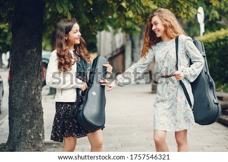 Girls in a summer park. Two ladies with a violin. Friends walking in a city