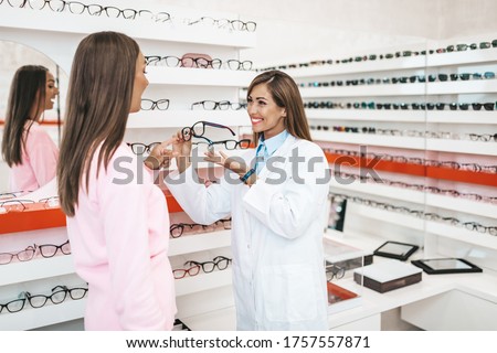 Middle age women seller and customer choosing new eyeglasses in modern optical store. Shopping concept.