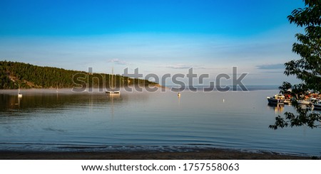 peaceful anchoring bay with a tiny bit of fog at summertime on a huge river in Tadoussac, Quebec, Canada during golden hour Royalty-Free Stock Photo #1757558063