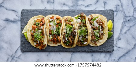 row of mexican street tacos on slate with carne asada and al pastor in corn tortilla