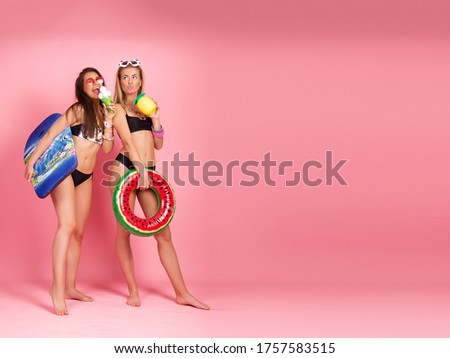 Two beautiful young women in bikini, beach summer tropical vibe, studio shot, isolated on pink background. Brunette and blond girl