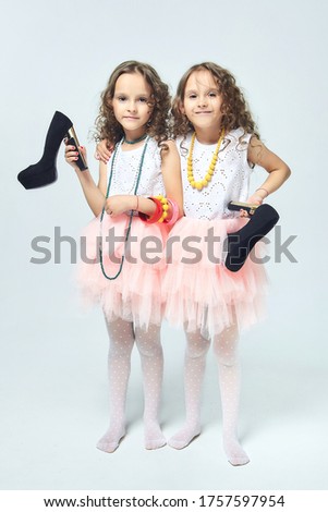two little girls play with their mother's high-heeled shoes. they pose and try to be adults.Studio, White back