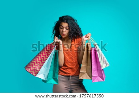 Curious and flirty dark skinned girl looking into one of the shoping bags she's holding checking her purchases. Royalty-Free Stock Photo #1757617550
