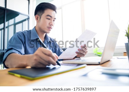 Working from home web designing graphical user interface UX UI, home office using computer laptop and pen sketching graphics tablet, using draft ideas and plans on paper drawing, asian man quarantine 