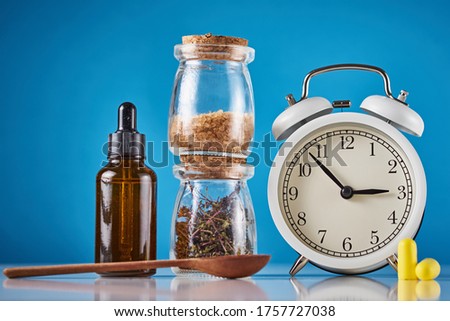 Herbal medicine for treat depression and insomnia concept. Alarm clock, medicine herbs and aromatherapy oil on blue background