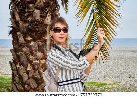Attractive beautiful young girl who is female photographer traveller with modern mirror camera near palm tree and sea beach background