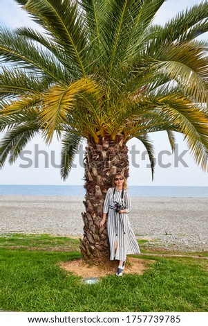 Attractive beautiful young girl who is female photographer traveller with modern mirror camera near palm tree and sea beach background