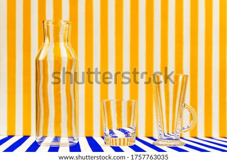 Transparent glassware-glasses and a bottle on a striped background.