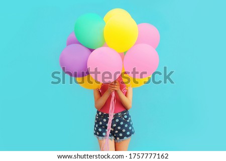 Festive image of unknown woman covering her head and holding in hands bunch of balloons on blue wall background