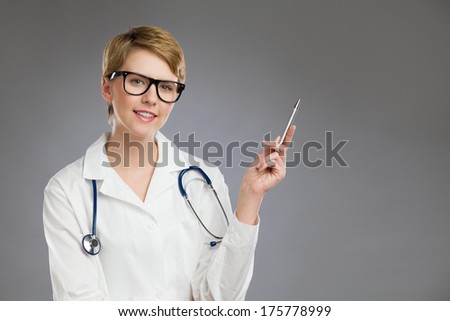Portrait of a female doctor pointing with pen. Waist up studio shot on gray background.